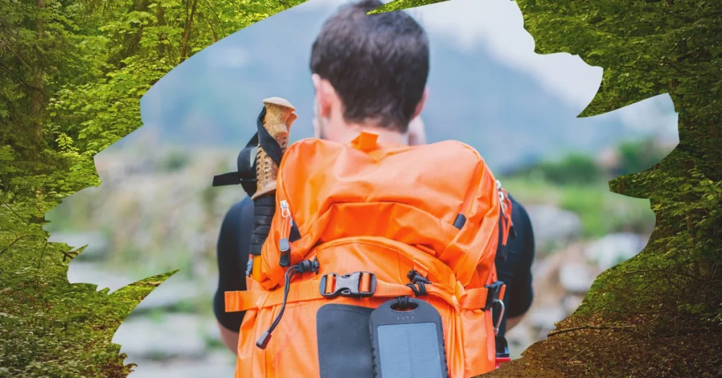 A traveler with an orange backpack hikes through a scenic mountain trail while using a solar-powered charger attached to the bag. The image is framed with green leaves, symbolizing eco-friendly travel.