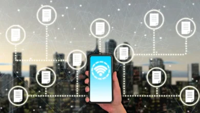 A hand holding a smartphone with a wireless icon on screen, surrounded by floating document icons symbolizing data transfer in a digital network over a city background.