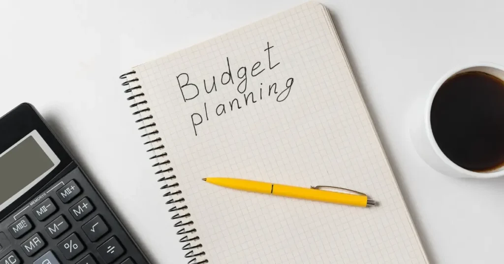A white desk setup featuring a notebook with "Budget planning" written on it, a yellow pen, calculator, and a cup of coffee—symbolizing smart spending decisions like choosing the best wireless earbuds under $50. The scene reflects thoughtful planning for tech buys, including budget earbuds 2025, cheap Bluetooth earbuds, and noise cancelling earbuds for affordable yet high-quality audio.
